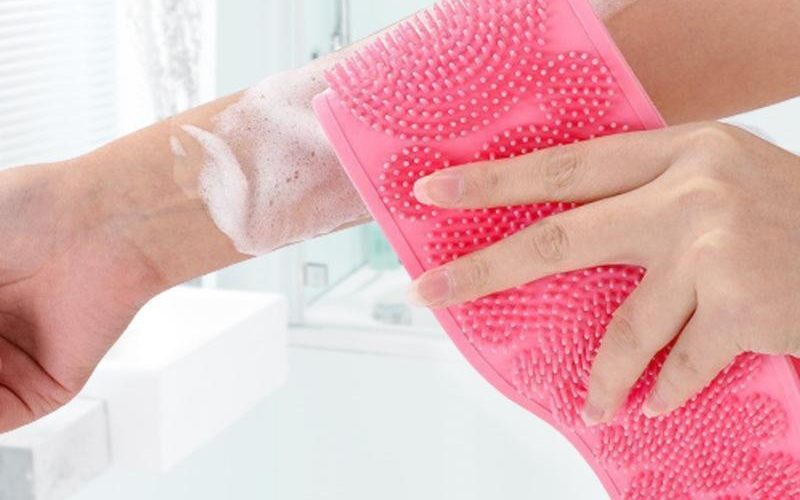 Pink silicone scrubber used with body wash on an arm